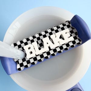 A white bowl with the name "BLAKE" written on it in large letters, placed on a blue surface.