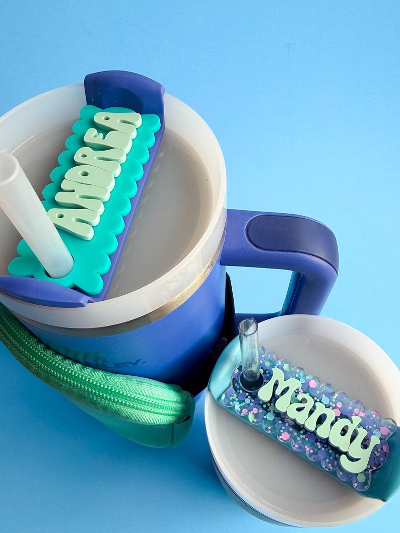 A blue and white sippy cup with a personalized name tag attached to it, sitting on a blue surface.