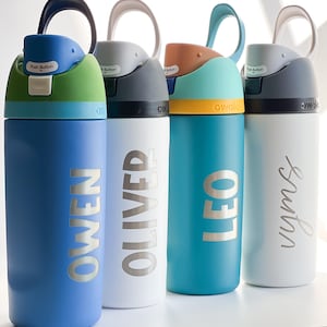 May include: Four colorful water bottles with names printed on them. The bottles are blue, white, teal, and light blue. Each bottle has a different colored lid and a handle. The names "Owen", "Oliver", "Leo", and "Sasha" are printed in silver.
