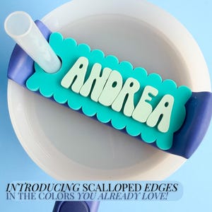 a scalloped edge nameplate with the name Andrea, placed on a white plate against a blue background.