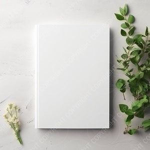 May include: A white blank book with a white background. Green leafy branches are on the right side of the image and white flowers are on the left side of the image.