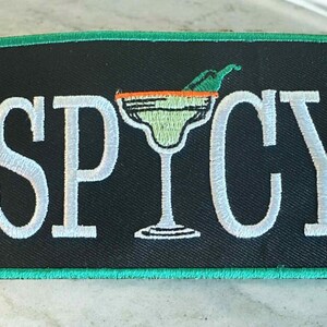 May include: Embroidered patch with the word "SPICY" in white capital letters. A green margarita glass with a green pepper garnish is in the center. The patch has a black background and a green border.