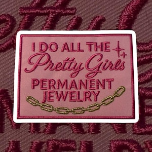 May include: A pink embroidered patch with the text "I DO ALL THE Pretty Girls PERMANENT JEWELRY" and a gold chain design. The patch has a white border and is set against a textured maroon background.