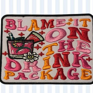 May include: Embroidered patch with the phrase "BLAME IT ON THE DRINK PACKAGE" in various colors. The patch features a cocktail illustration with a watermelon slice and a flower.