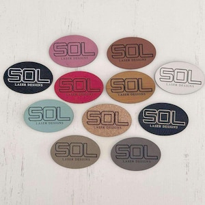 May include: Ten oval-shaped leather labels with the text "SOL LASER DESIGNS" in a black font. The labels are in various colors, including pink, brown, white, red, beige, teal, and gray.