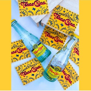 May include: Two glass bottles of Topo Chico mineral water with yellow caps and labels, surrounded by yellow coasters. The coasters have a scalloped edge and read "Texas Chica" and "Made in Texas" in red and blue.