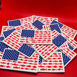 May include: A stack of white American flag-themed coasters with red and blue stars and stripes. The stripes are made up of red fish silhouettes.
