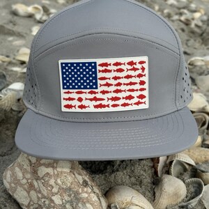 May include: A gray and white baseball cap with a red, white, and blue American flag design featuring a row of red fish. The flag is on the front of the cap.