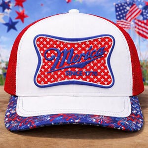 May include: A white and red trucker hat with a patriotic design. The front features a blue and red patch with the word "Merica" and "Since 1776". The brim has a red, white, and blue firework pattern.