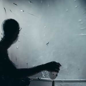 May include: A silhouette of a person holding a white ball in front of a blurred, grey background with streaks of light.