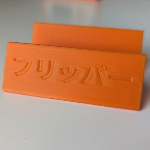 Puede incluir: Señal de plástico naranja con el texto japonés "フリーパー" en relieve en la superficie.