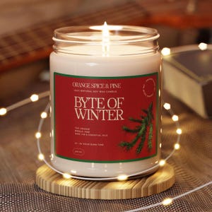 May include: A red and green candle jar with the text "Orange Spice & Pine 100% Natural Soy Wax Candle Byte of Winter" and "Top Orange Middle Pine Base Fir & Essential Oils 50-55 Hour Burn Time".