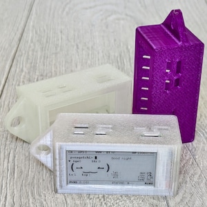 May include: Three 3D-printed house-shaped electronic device enclosures. One is clear, one is white, and the other is purple. The front-most device displays text including "Good night." The devices have a loop for hanging.