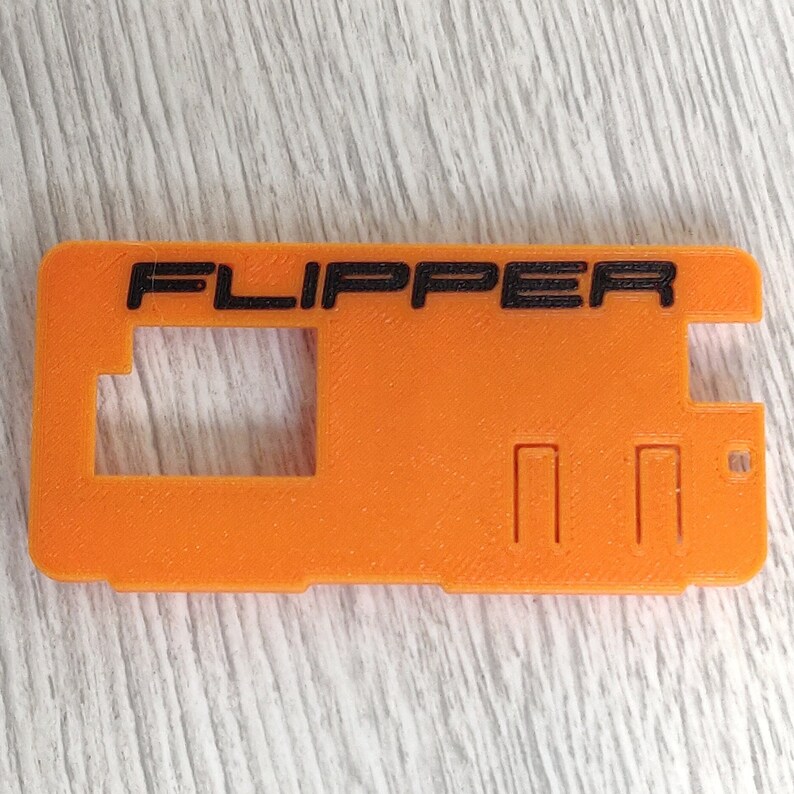以下が含まれることがあります： オレンジ色のプラスチックケースに黒い文字で「FLIPPER」と印刷されています。ケースには長方形の切り抜きが3つと、より大きな長方形の切り抜きが1つあります。