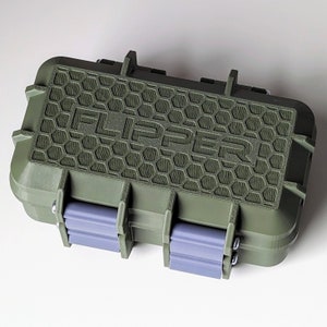 May include: An olive green rectangular case with the word "FLIPPER" embossed on the top. The top features a honeycomb pattern. The case has two grey latches and hinges. The case is designed to protect its contents.