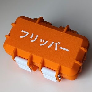 May include: An orange plastic case with a white label that says "フリップバー". The case has a textured surface and white latches.