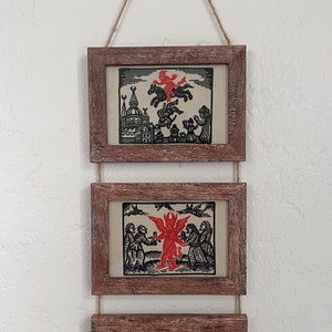 May include: Three framed wood prints with black and red illustrations of a devil figure. The top print shows the devil riding a horse above a city. The middle print shows the devil holding a small figure. The bottom print shows the devil surrounded by other figures.