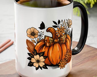 May include: White ceramic mug with a black handle and rim, featuring a vibrant orange pumpkin design with floral accents and a butterfly. The mug is filled with a dark liquid, perfect for fall beverages.