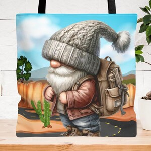 Op de afbeelding: Een fantasievolle tote bag met een cartoon-dwerg die een grijze gebreide muts en een bruin jack draagt. De dwerg draagt een bruine rugzak en loopt op een woestijnweg met een cactus op de achtergrond.