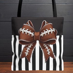 May include: Tote bag with a football-themed bow design. The bow is brown with white stitching, set against a black and white striped background. The bag has black handles and the text "SOLD SEPARATELY" at the bottom.