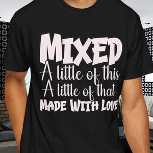 May include: Black t-shirt with the word "MIXED" in large white letters. Below, the text reads "A little of this, A little of that, MADE WITH LOVE" in a white, handwritten-style font. The shirt is worn by a person.