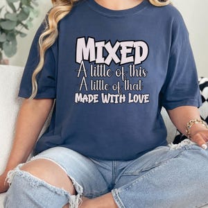 May include: A navy blue t-shirt with the word "MIXED" in a white and pink font. Below the word "MIXED" is the text "A little of this, A little of that, MADE WITH LOVE" in a white font. The shirt is worn by a person.