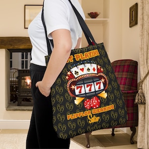 May include: Black tote bag with a colorful slot machine graphic and the text "Not Playing Flip Flop Wearing Sister".
