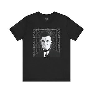 May include: Black t-shirt with a white image of a man with a rune on his forehead. The image is surrounded by a decorative border.