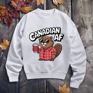Puede incluir: Sudadera blanca con un castor de dibujos animados que lleva gafas de sol y sostiene una taza de café. El texto "CANADIAN AF" está impreso en la sudadera.