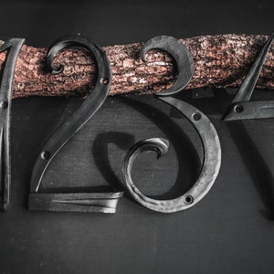 Könnte beinhalten: Schwarze Hausnummern aus Metall 1, 2, 3 und 4. Die Zahlen befinden sich auf einem Hintergrund aus Holzscheiten.