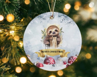May include: A round white Christmas ornament with a cute cartoon sloth holding onto a tree branch. The ornament has a gold ribbon and the words "Merry Christmas" written on it. There are red and silver ornaments surrounding the sloth.