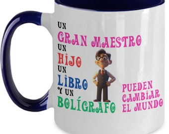 May include: White ceramic coffee mug with a blue rim and handle. The mug features a cartoon character and the text "Un Gran Maestro Un Hijo Un Libro Y Un Boligrafo Pueden Cambiar El Mundo".