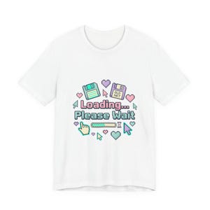 Könnte beinhalten: Weißes T-Shirt mit Retro-Grafik. Das Design zeigt einen Ladebildschirm mit Diskette, Herzen und dem Text "Loading... Please Wait". Die Grafik ist in Pastellfarben gehalten.