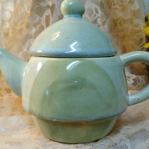 May include: A green and blue ceramic teapot with a lid. The teapot has a rounded body and a spout on one side. The lid has a knob on top.