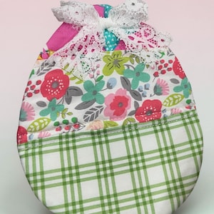 May include: A fabric egg-shaped item with a floral pattern in pink, red, green, and blue, topped with a white lace bow. The bottom half features a green and white plaid design.