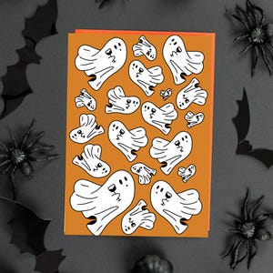 Peut inclure: Une carte de vœux rectangulaire avec un fond orange ornée d'un motif répétitif de fantômes blancs en dessin animé. Chaque fantôme est souligné en noir et tient un petit verre à vin noir. Les fantômes varient en taille et en orientation.