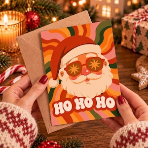 Può includere: Un biglietto d'auguri con un'illustrazione grafica di Babbo Natale che indossa occhiali da sole a forma di stella. Lo sfondo è composto da strisce ondulate multicolori arancioni, rosa e verdi. Il testo HO HO HO è stampato in bianco in basso.