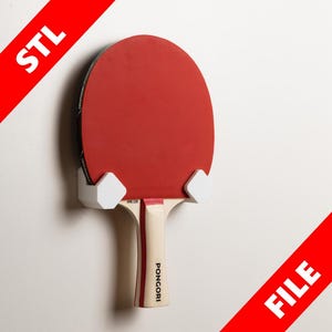 May include: White 3D printed wall mount for a ping pong paddle. The paddle is red with a black and white handle and the text "PONGORI" printed on the handle.