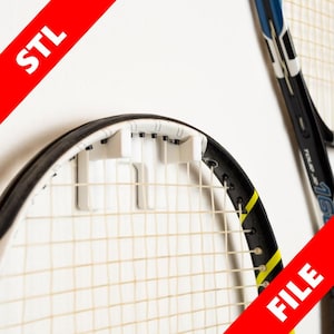 Puede incluir: Soporte de pared de plástico blanco para colgar una raqueta de tenis. El soporte tiene cuatro ganchos y está fijado a una pared blanca. Una raqueta de tenis está colgada del soporte.