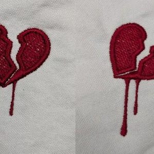 May include: Two embroidered images of a broken heart with red thread dripping down from the break. The hearts are on a white fabric background.