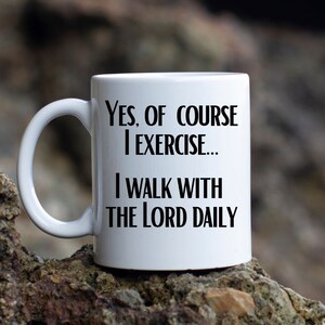 May include: White ceramic mug with a curved handle. The mug features black text that reads: "Yes, of course I exercise... I walk with the Lord daily."