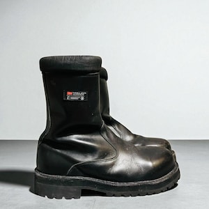 Könnte beinhalten: Schwarze Arbeitsstiefel mit einer dicken, profilierten Sohle. Die Stiefel haben eine runde Spitze und einen gepolsterten Kragen. Ein kleines Etikett mit dem Text "3M Thinsulate" ist seitlich sichtbar.