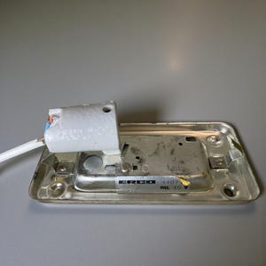 May include: A rectangular, silver light fitting base with a white ceramic lamp holder. The base has a label that reads "ERCO 4407 max. 40 W". A white electrical cord extends from the lamp holder.