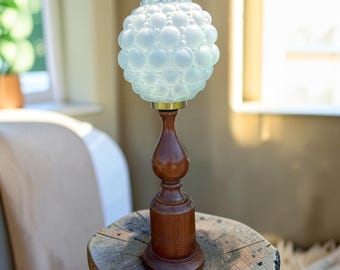 May include: A table lamp featuring a spherical, white, bubble-textured glass shade mounted on a turned, dark brown wooden base. The lamp has a slender, contoured stem that connects the glass globe to the cylindrical wooden pedestal stand.