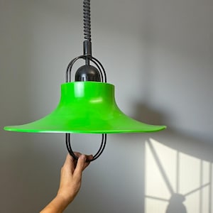 May include: A bright green, retro-style pendant light with a wide, flared shade. The light fixture has a black metal frame and a coiled cord. The shade is a vibrant, glossy green, and the overall design suggests a mid-century modern aesthetic.