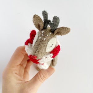 May include: A handmade felt reindeer with a red and white scarf. The reindeer has brown fur, gray antlers, and white spots. The reindeer is a festive holiday decoration.