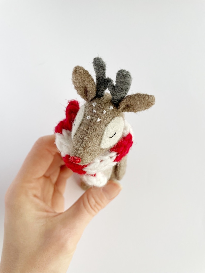 May include: A handmade felt reindeer with a red and white scarf. The reindeer has brown fur, gray antlers, and white spots. The reindeer is a festive holiday decoration.