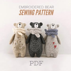 Puede incluir: Tres osos de peluche con detalles bordados y bufandas de punto. El oso izquierdo es beige con margaritas blancas, el central es gris oscuro con puntadas blancas y el derecho es gris claro con dos corazones rojos. El texto dice EMBROIDERED BEAR SEWING PATTERN PDF.