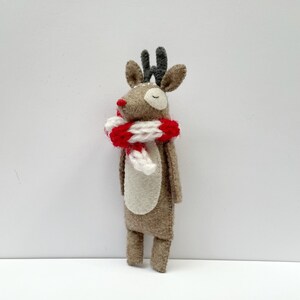May include: A handmade felt reindeer figurine with a red and white striped scarf. The reindeer has brown fur, a white belly, and small antlers. The figurine is a festive decoration for the holiday season.