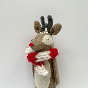 May include: A handmade felt reindeer with a red nose, gray antlers, and a red and white striped scarf. The reindeer has closed eyes and small white details. The overall design is whimsical and festive.